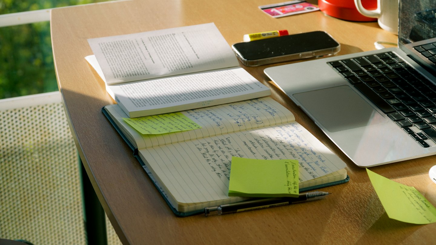 Silver laptop and notebook on a cluttered wooden desk.